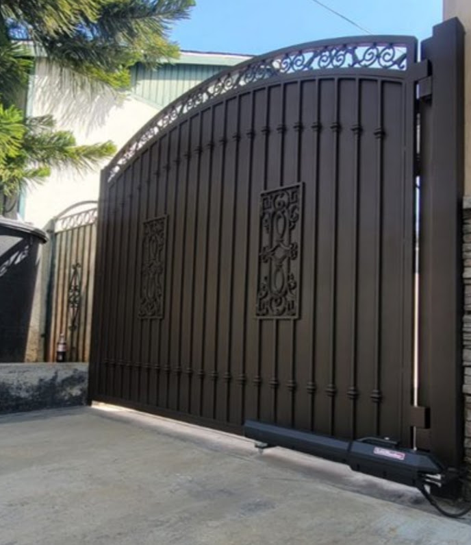 Bronze wrought iron swing gate with an arched top, scrollwork panel and cast medallion inserts, with a black linear swing operator along the bottom rail