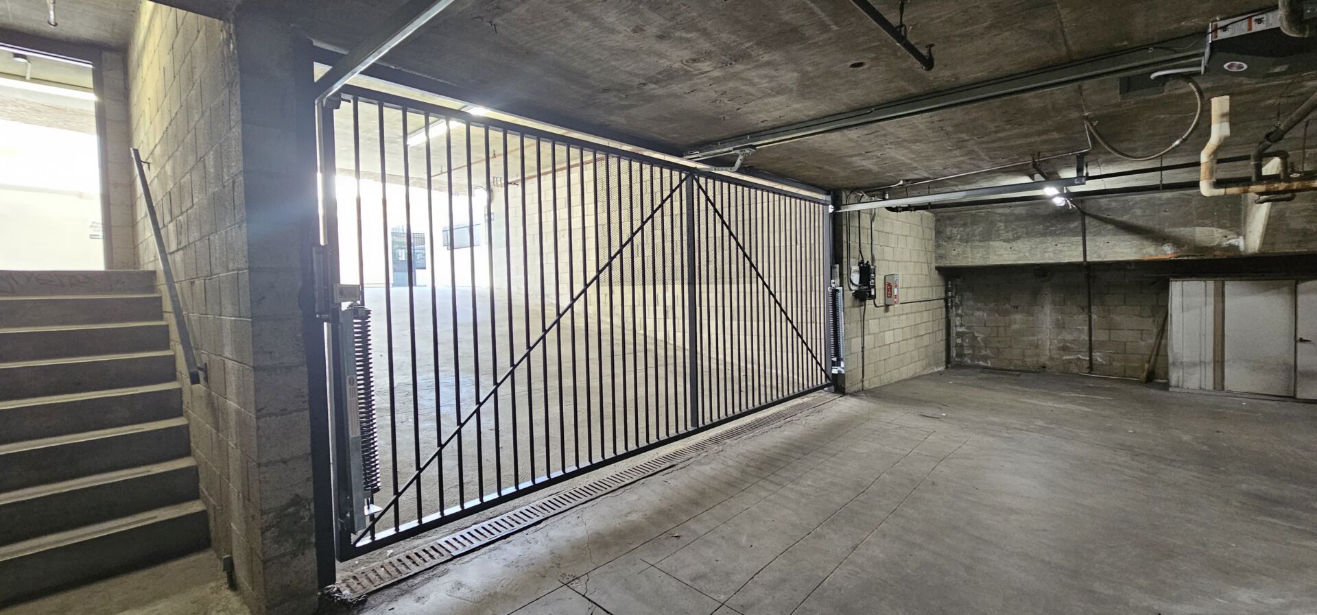 Gate Repair in Sherman Oaks, CA 20 Barred steel sliding security gate on a floor track inside an underground parking garage, with a stairwell alongside