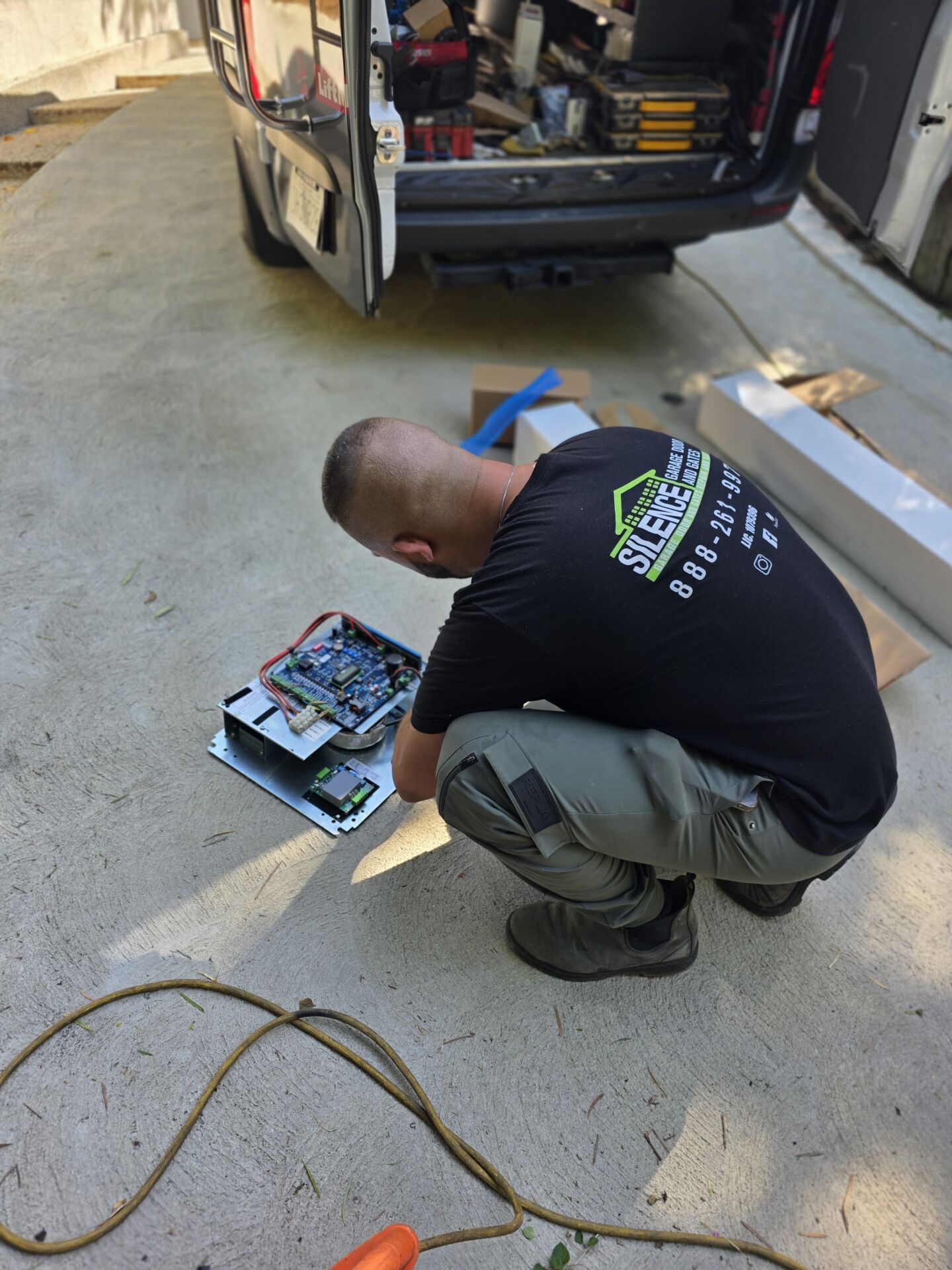 Gate Repair in Sherman Oaks, CA 8 Technician kneeling on the ground working on a gate control board laid out beside an open service van