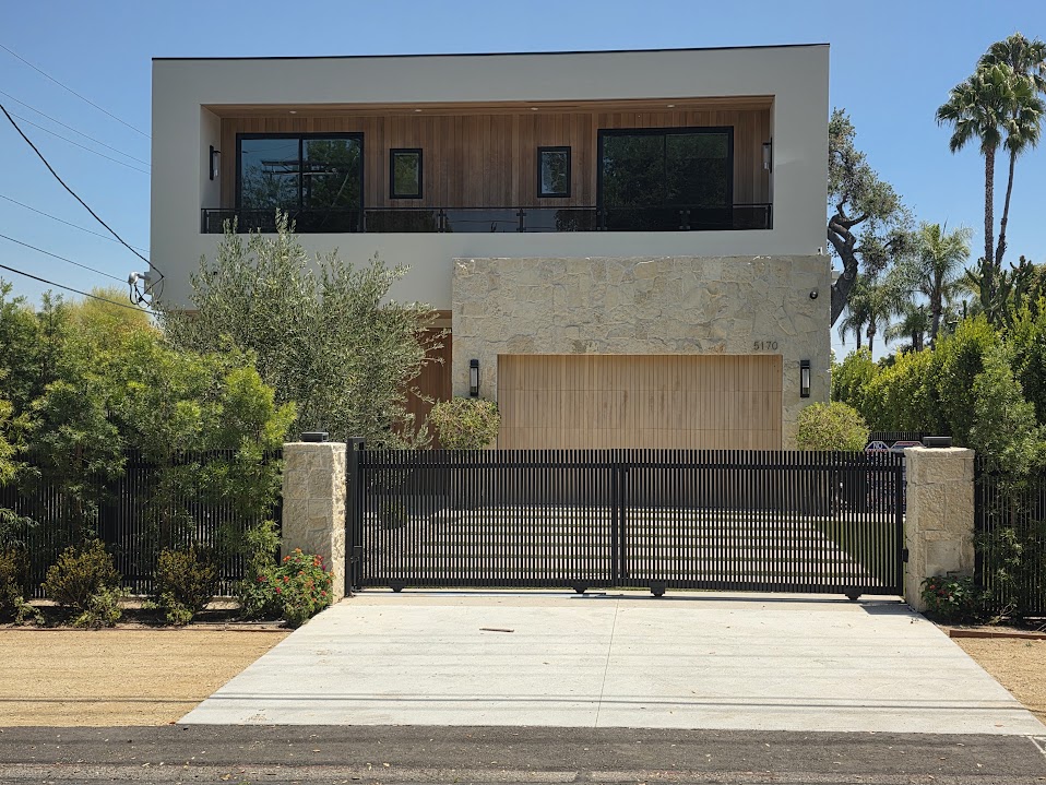 Gate Repair in Sherman Oaks, CA 13 Black vertical picket double driveway gate closed between stone-clad columns in front of a modern two-storey house