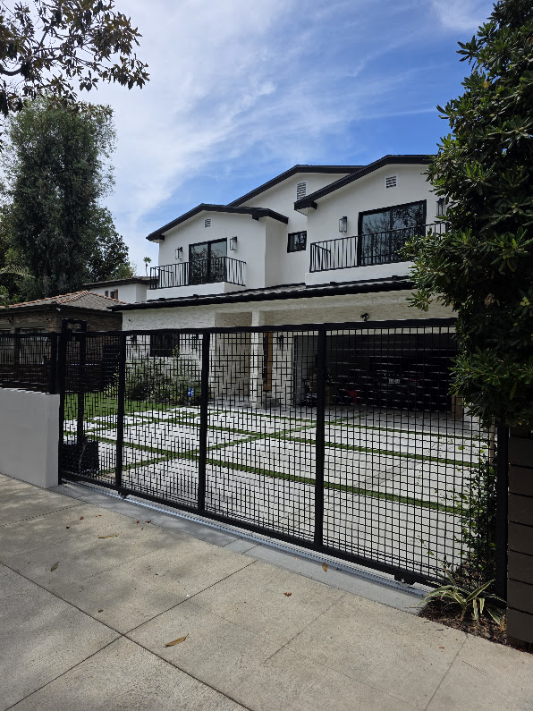Gate Repair in Sherman Oaks, CA 9 Black steel mesh sliding gate closed across a ribbon driveway on a bottom track, with a two-storey white house behind